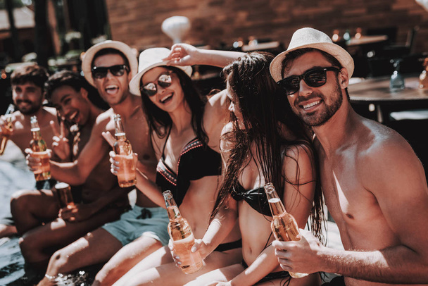 Young Friends with Alcoholic Drinks at Poolside. Group of Young Smiling People holding Bottles of Beer and having Fun at Poolside. Happy Friends Enoying Pool Party. Summer Vacation Concept - Valokuva, kuva