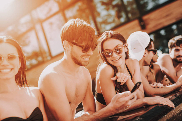 Young Smiling Friends using Smartphone at Poolside. Group of Young Happy People Talking and using Cellphones at Poolside of Outdoor Hotel Swimming Pool. Summer Vacation Concept. Pool Party - Fotoğraf, Görsel