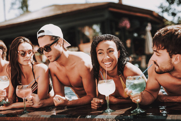 Young Smiling Friends with Cocktails at Poolside. Group of Young Happy People holding Glasses with Colorful Alcoholoc Drinks at Poolside. Happy Friends Enoying Pool Party. Summer Vacation Concept - 写真・画像