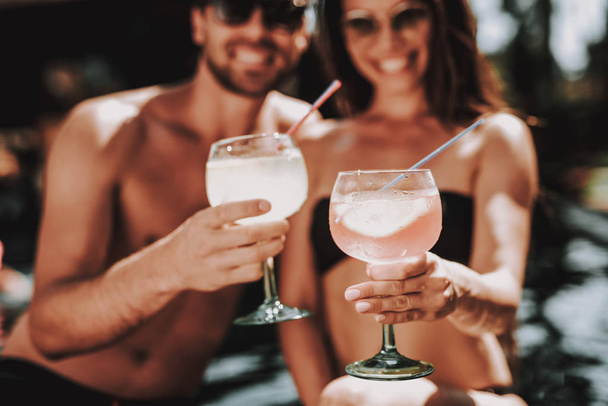 Smiling Couple Drinking Cocktails at Poolside. Beautiful Young Couple holding Glasses with Alcoholic Drinks and having Fun at Poolside. Happy Friends Enoying Pool Party. Summer Vacation Concept - Φωτογραφία, εικόνα