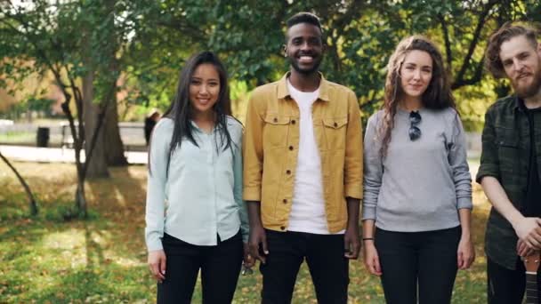 Slow motion portret van multiraciale groep van studenten meisjes en jongens permanent buitenshuis samen en op zoek naar camera met happy glimlach. Natuur en vriendschap concept. - Video