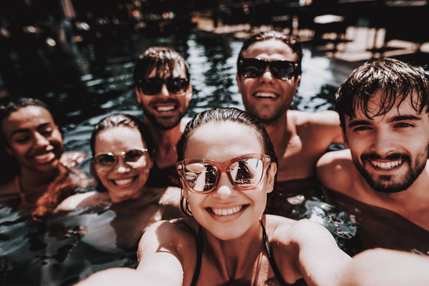 Young Happy Friends in Outdoor Swimming Pool. Group of Young Smiling People wearing Sunglasses having Fun Together by Swimming in Hotel Pool. Friends Enoying Pool Party. Summer Vacation Concept - Фото, зображення