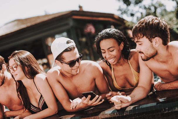 Jovens amigos sorridentes usando Smartphone na piscina. Grupo de Jovens Felizes Conversando e usando Celulares na beira da piscina exterior do Hotel. Conceito de férias de verão. Parte da piscina
 - Foto, Imagem