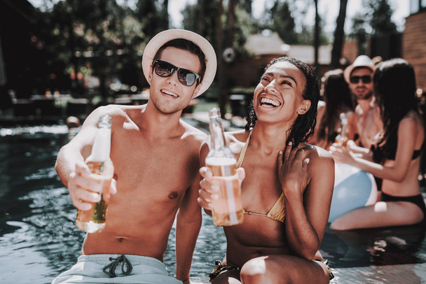 Smiling Couple with Alcoholic Drinks at Poolside. Beautiful Black Woman and Young Man holding Bottles of Beer and having Fun at Poolside. Happy Friends Enoying Pool Party. Summer Vacation Concept - Foto, imagen