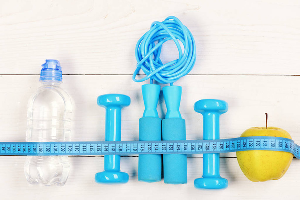 Barbells, jump rope, bottle and apple on wooden background - Photo, image