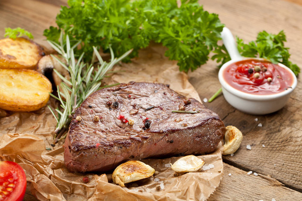Vue aérienne d'un délicieux steak de boeuf grillé avec pommes de terre rôties et salade d'herbes vertes fraîches sur une vieille table en bois
 - Photo, image