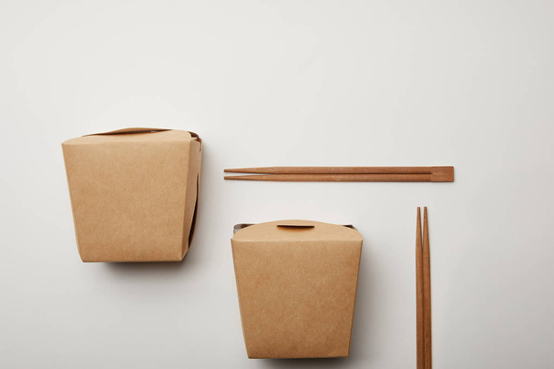 flache Lage mit arrangierten Wok-Schachteln und Essstäbchen auf weißer Oberfläche, minimalistisches Konzept  - Foto, Bild