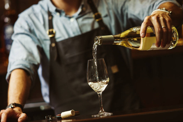 Male sommelier pouring white wine into long-stemmed wineglasses. - Foto, Imagen