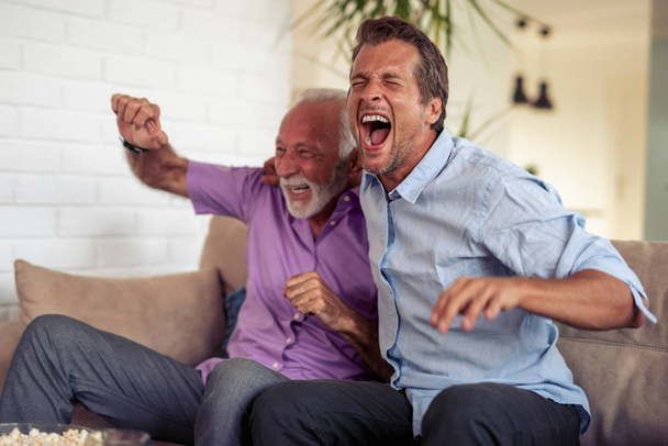 Двоє чоловіків дивляться футбол, п'ють пиво і їдять попкорн вдома
. - Фото, зображення