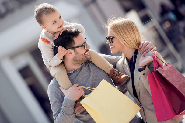 Gelukkige familie met kleine zoon en boodschappentassen wandelen in de stad - Foto, afbeelding