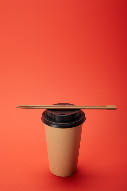 Close-up van eetstokjes op papier kopje koffie op rood, minimalistische concept - Foto, afbeelding