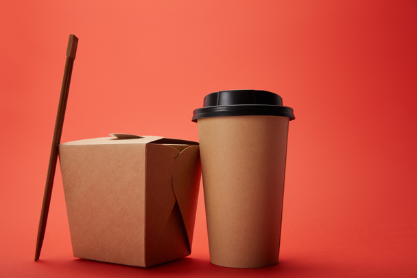vue rapprochée de la boîte à nouilles, tasse de café en papier avec baguettes sur rouge, concept minimaliste
 - Photo, image