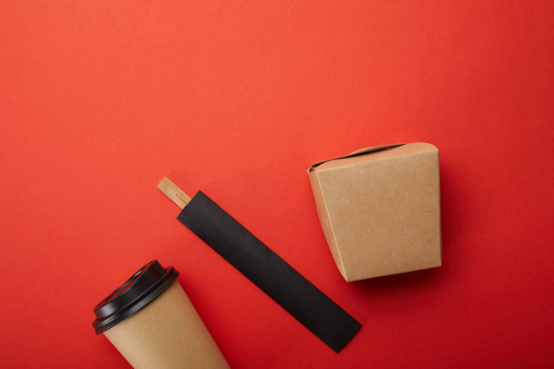 Draufsicht auf Nudelbox, Pappbecher Kaffee mit Stäbchen auf Rot, minimalistisches Konzept - Foto, Bild