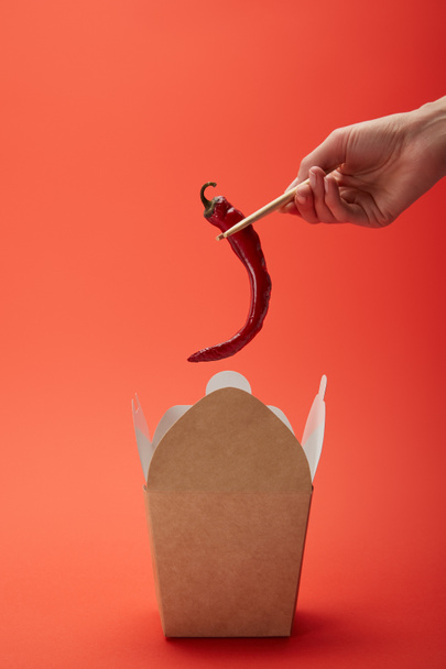 cropped image of woman holding chili pepper in chopsticks above noodle box on red  - Photo, Image