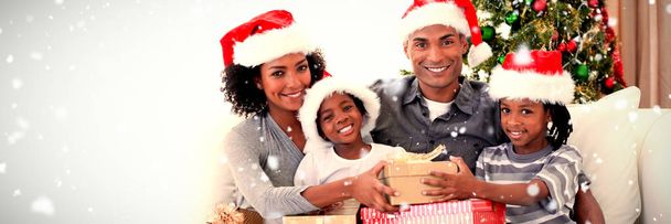 Smiling family sharing Christmas presents against snow falling - Photo, image