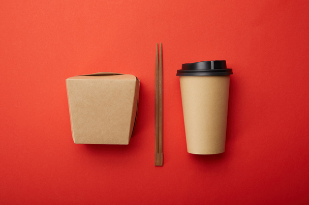 επίπεδη θέσει με chopsticks, noodle κουτί και μίας χρήσης φλιτζάνι καφέ κόκκινο επιφάνεια, μινιμαλιστική έννοια  - Φωτογραφία, εικόνα