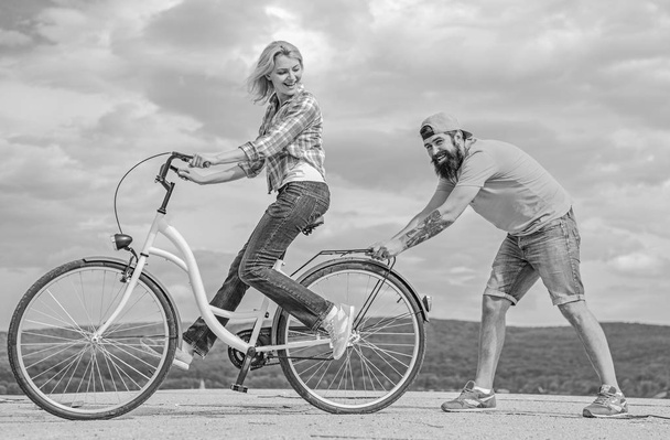 Teach adult to ride bike. Man helps keep balance and ride bike. Find balance. Woman rides bicycle sky background. How to learn to ride bike as an adult. Girl cycling while boyfriend support her - Foto, imagen