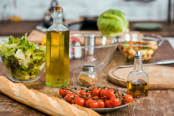 rijpe verse groenten voor salade, fles olijfolie en stokbrood op tafelblad in keuken - Foto, afbeelding