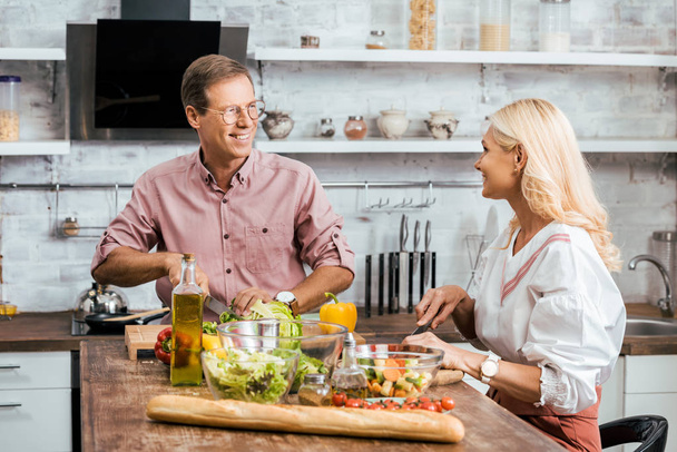smiling couple preparing salad for dinner together in kitchen, looking at each other - Фото, зображення