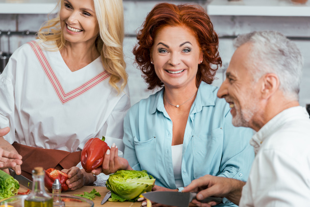laughing mature friends preparing salad for dinner at home - Photo, Image