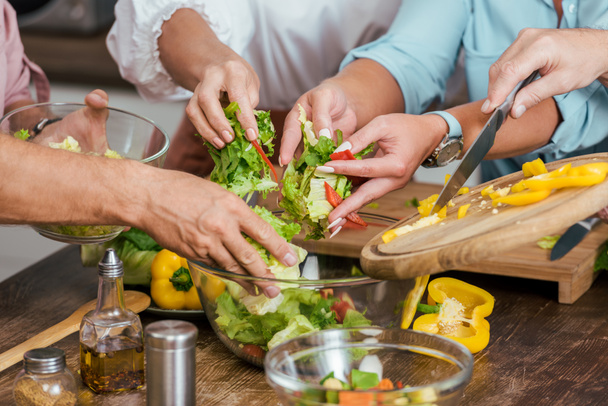 abgeschnittenes Bild von reifen Freunden, die zu Hause Salat für das Abendessen zubereiten - Foto, Bild