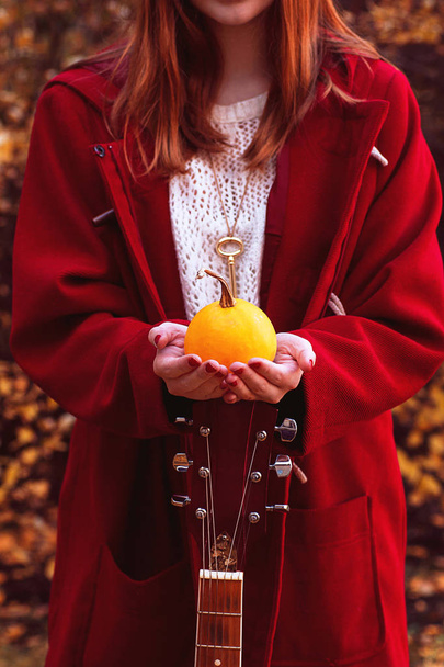 A menina está segurando uma pequena abóbora com uma guitarra vermelha
 - Foto, Imagem