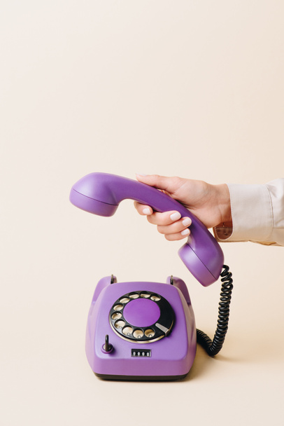 cropped view of woman holding phone tube of purple rotary phone on beige - Foto, Imagen