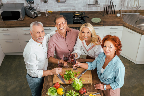 high angle view of happy old friends clinking with wineglasses in kitchen - Photo, Image