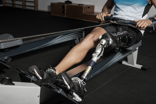 Gesichtsloser Schuss auf Sportler beim Training mit Beinprothese auf Rudergerät im Fitnessstudio - Foto, Bild