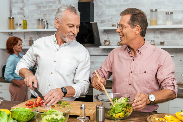 красивые улыбающиеся мужчины готовят салат к ужину дома
 - Фото, изображение