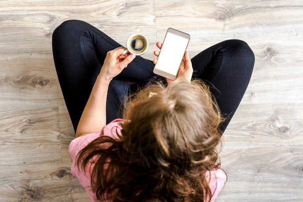 Woman using mobile phone in hand and making coffee time. Modern smartphone with white screen. Hipster person working home or online shopping concept. - Photo, image