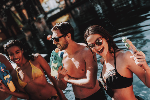 Young Smiling People in Pool with Water guns. Young Happy Friends standing Together with Colorful Water guns in Outdoor Swimming Pool. Friends at Pool Party. Summer Vacation Concept - Foto, immagini