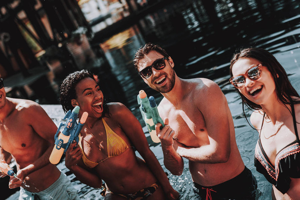 Young Smiling People in Pool with Water guns. Young Happy Friends standing Together with Colorful Water guns in Outdoor Swimming Pool. Friends at Pool Party. Summer Vacation Concept - Foto, Bild