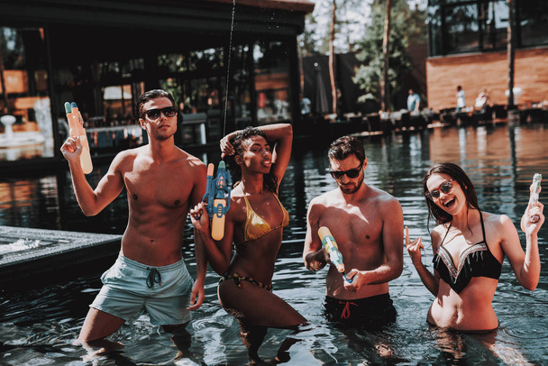 Young Smiling People in Pool with Water guns. Young Happy Friends standing Together with Colorful Water guns in Outdoor Swimming Pool. Friends at Pool Party. Summer Vacation Concept - Zdjęcie, obraz