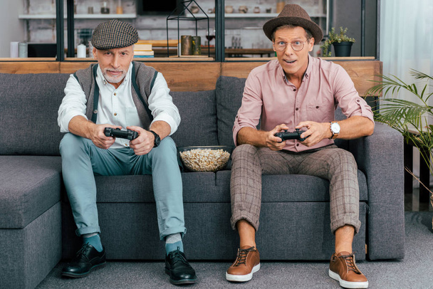 knappe volwassen mannen met behulp van de joysticks en camera kijken samen zittend op de Bank  - Foto, afbeelding
