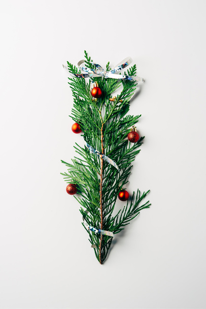 bovenaanzicht van groene pijnbomen tak versierd met Kerstmis speelgoed en lint als kerstboom op witte achtergrond - Foto, afbeelding