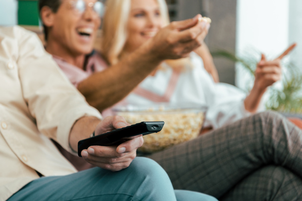 cropped shot of mature friends using remote controller and eating popcorn while watching tv together - Photo, Image