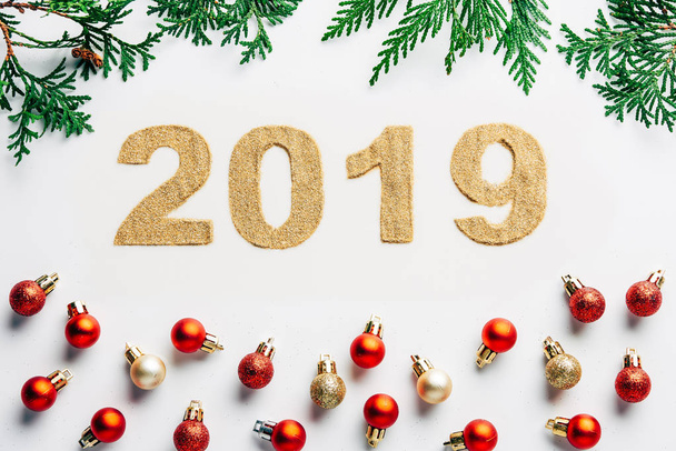 top view of 2019 year sign, pine tree branches and christmas balls on white background - Fotó, kép