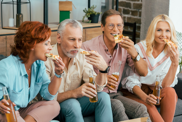 two mature couples drinking beer and eating pizza together at home - Zdjęcie, obraz