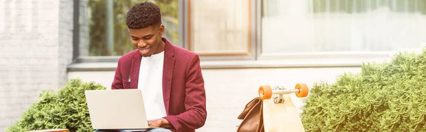 широкий тонований знімок щасливого афроамериканського фрілансера, використовуючи ноутбук на вулиці
 - Фото, зображення