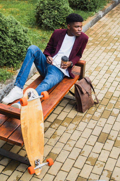 stijlvolle jongeman met papieren kopje koffie en brillen zittend op de Bank - Foto, afbeelding