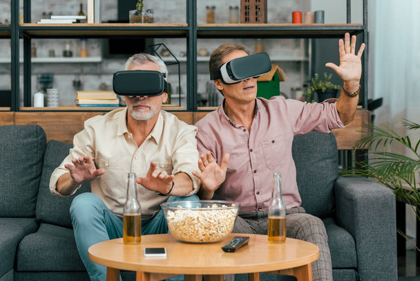 mature male friends sitting on couch and using virtual reality headsets - Foto, imagen