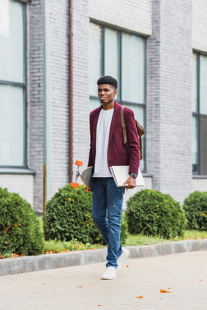 joven estudiante guapo con mochila y monopatín caminando por la calle
  - Foto, Imagen