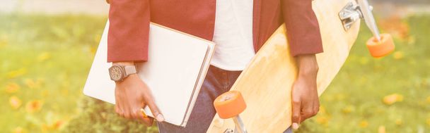 recortado amplia toma de elegante estudiante con cuadernos y monopatín de pie en la calle
 - Foto, Imagen
