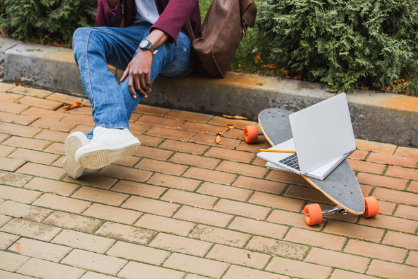 обрізаний знімок фрілансера, що сидить на бордюрі на вулиці біля ноутбука на скейтборді
 - Фото, зображення