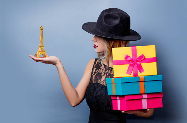 Retrato de una chica de estilo joven en vestido negro y sombrero con regalos y recuerdo de la torre Eiffel sobre fondo gris
 - Foto, imagen