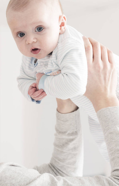 Vertical view of mother holding up cute infant in striped rompers - Фото, зображення