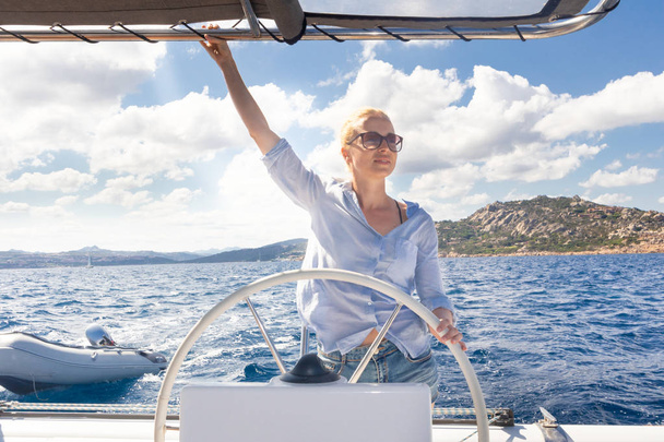 attraktive blonde Skipperin steuert das schicke Katamaran-Segelboot an einem sonnigen Sommertag auf ruhigem, blauem Meerwasser. - Foto, Bild