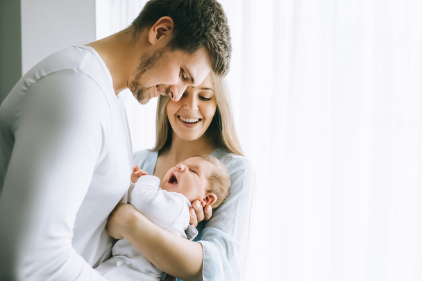 sonriente familia llevando pequeño bebé niño delante de cortinas en casa
 - Foto, imagen