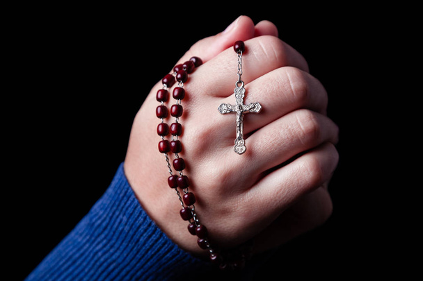 Frauenhände beten mit einem Rosenkranz mit Jesuschrist im Kreuz oder Kruzifix auf schwarzem Hintergrund. Frau mit christlich-katholischem Glauben - Foto, Bild